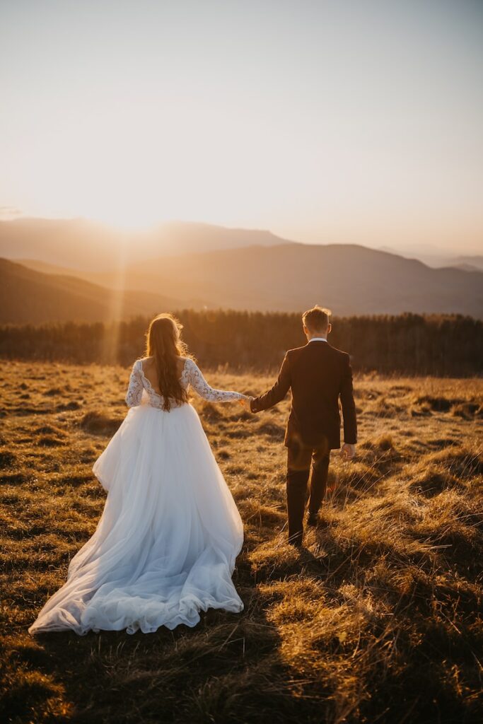 homme et femme en robe de mariée marchant sur un champ d'herbe brune pendant la journée